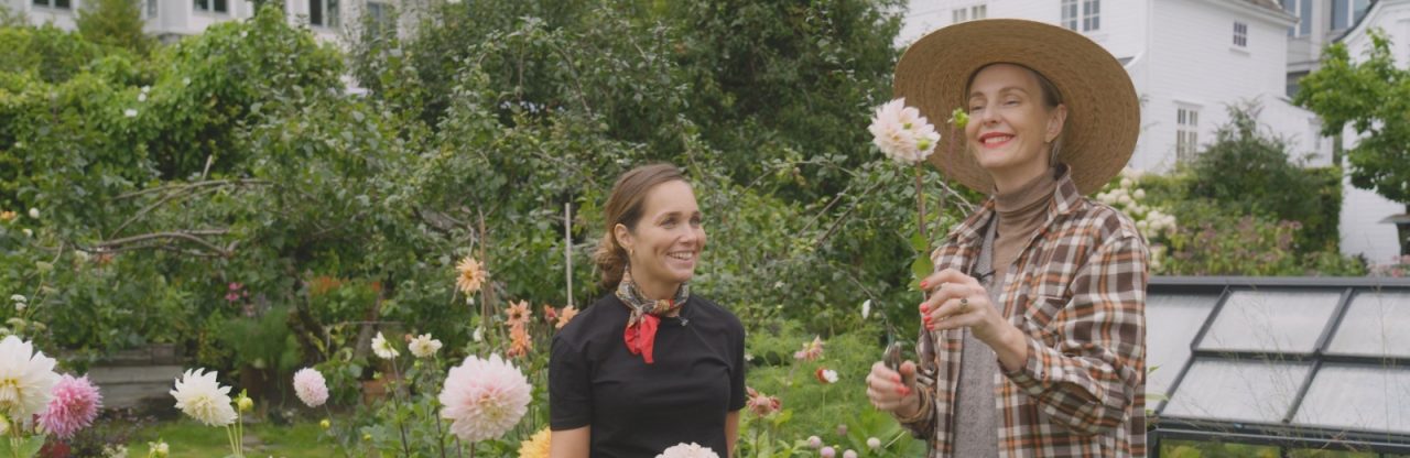 To damer som lukter på blomster i hagen.