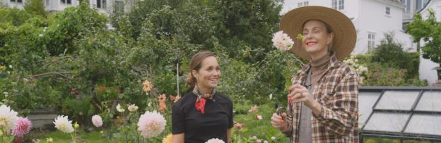 To damer som lukter på blomster i hagen.
